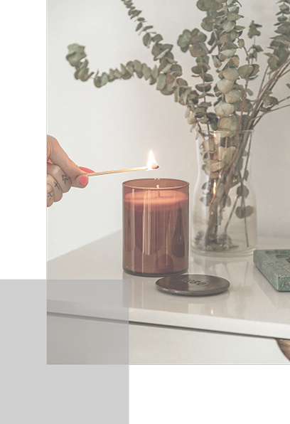 茶色のガラス容器のキャンドルに、手に持ったマッチで火を灯そうとしている落ち着いた室内の様子
