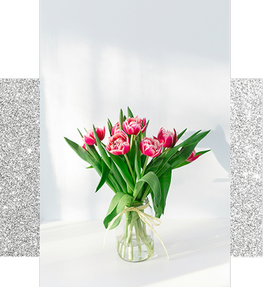 白いテーブルの上に置かれた花瓶入りのチューリップ。明るい日差しを受け、春らしい華やかさが伝わる静物写真。