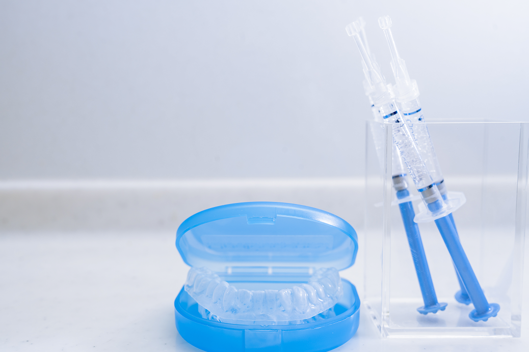 透明な歯列用マウスピースを収めたブルーのケースと、青い液体が入った注射器型ツールを清潔な背景で撮影
